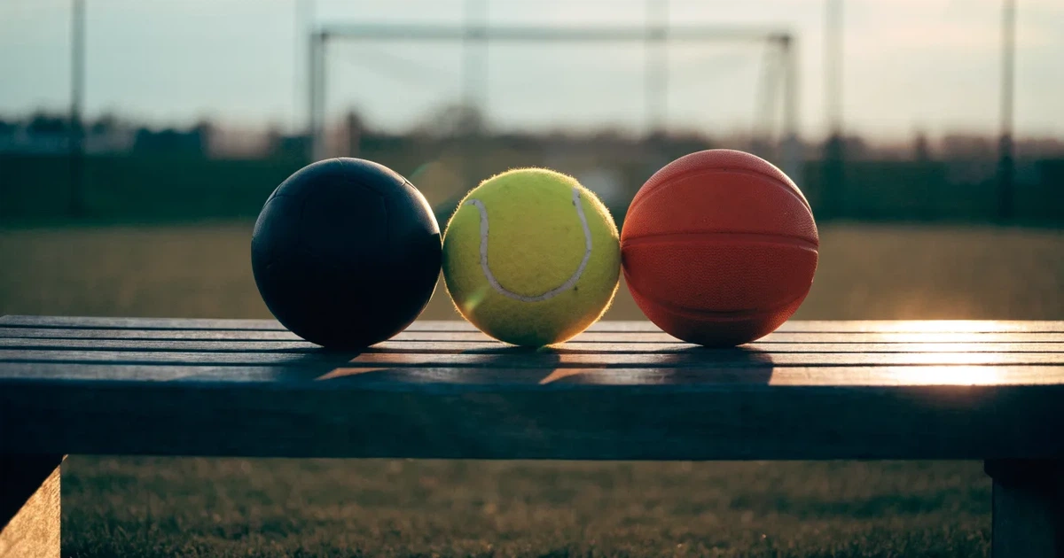 Tre palloni di sport diversi allineati uno accanto all'altro su una panca di legno