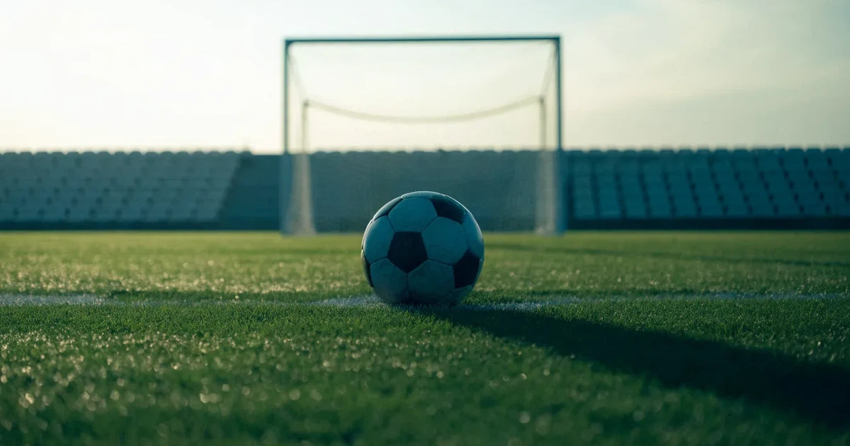 Un pallone da calcio sul dischetto del centrocampo di un prato, alla luce del mattino